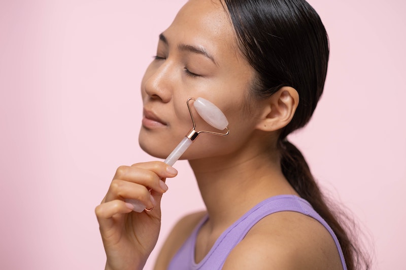 An Asian woman using a rose quartz face roller on her cheek