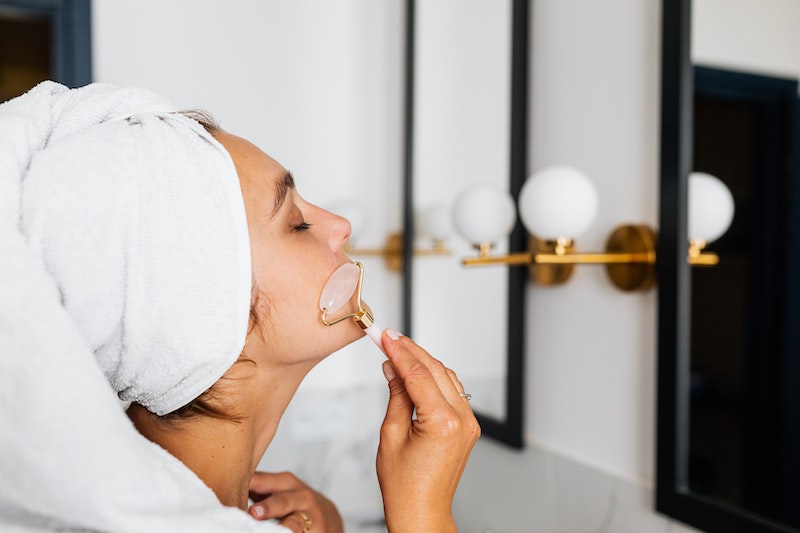 A woman using a rose quartz facial roller in front of a mirror after a shower