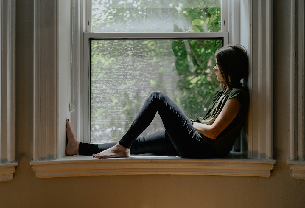 woman reflecting on identity in motherhood sitting on window sill