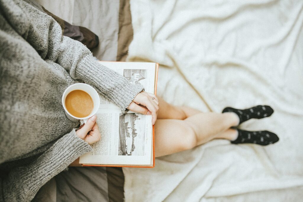 self care mothers small moments woman holding a cup of coffee at right hand and reading book on her lap while holding it open with her left hand in a well-lit room