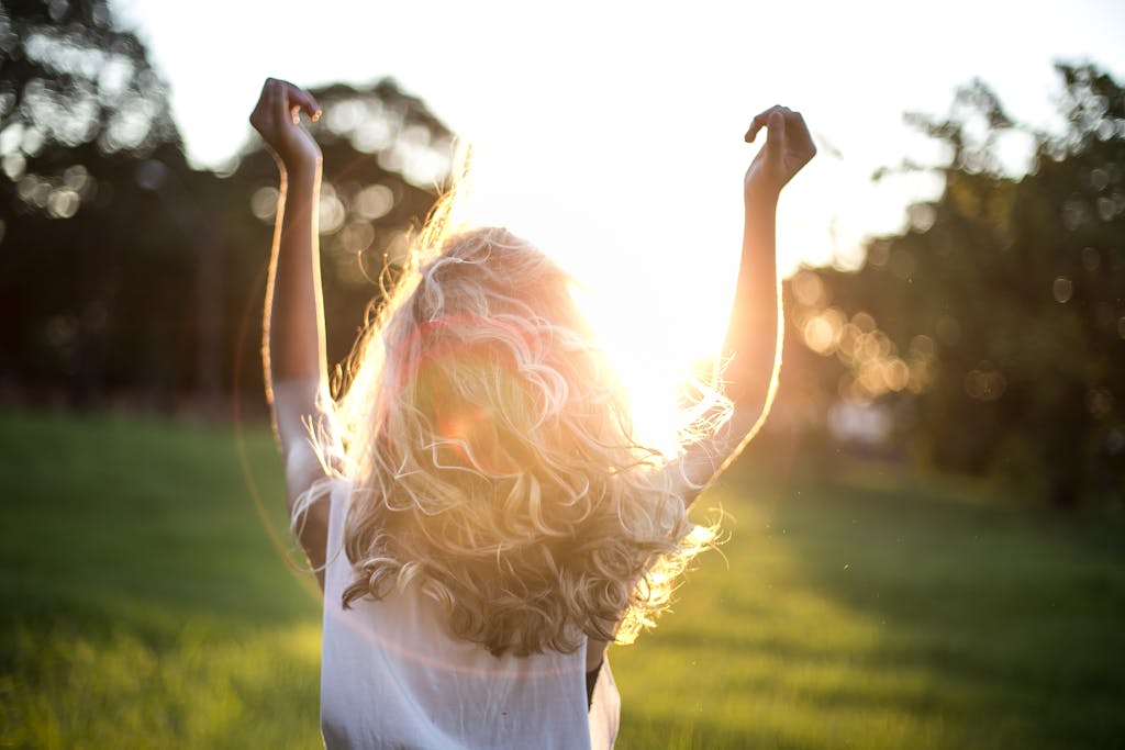 A woman reclaiming energy with outstretched arms celebrates the sunset in a grassy field, capturing the essence of freedom and joy.