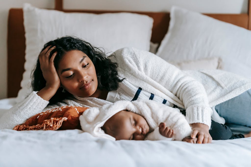 Emotional moments for moms Calm young black woman with dark hair in casual clothes lying on bed with adorable sleeping baby in daylight