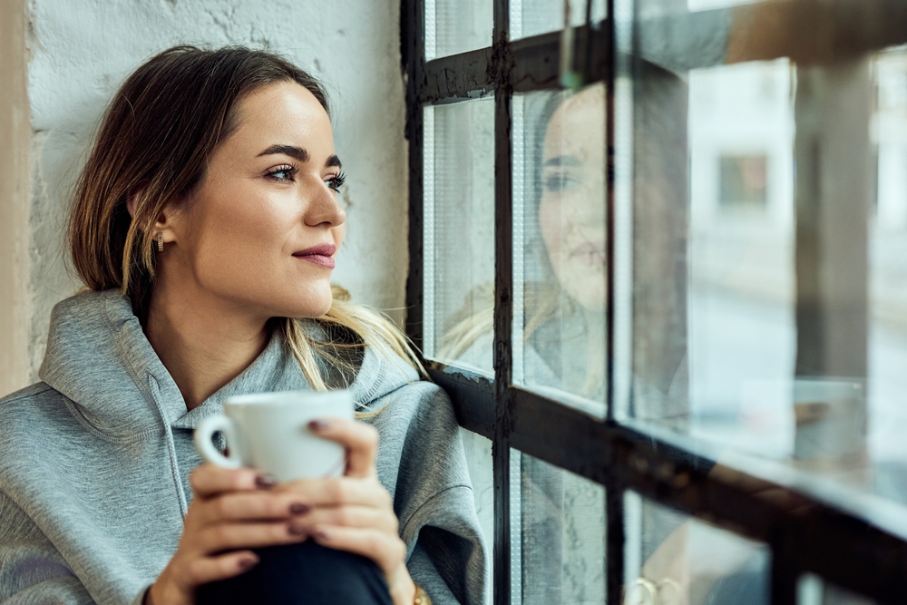 woman reflecting on identity in motherhood by window