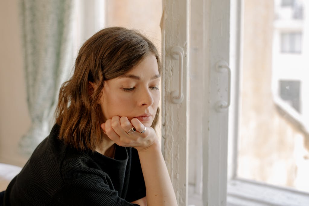 postpartum recovery for Young woman looking thoughtful while sitting by a window indoors. 