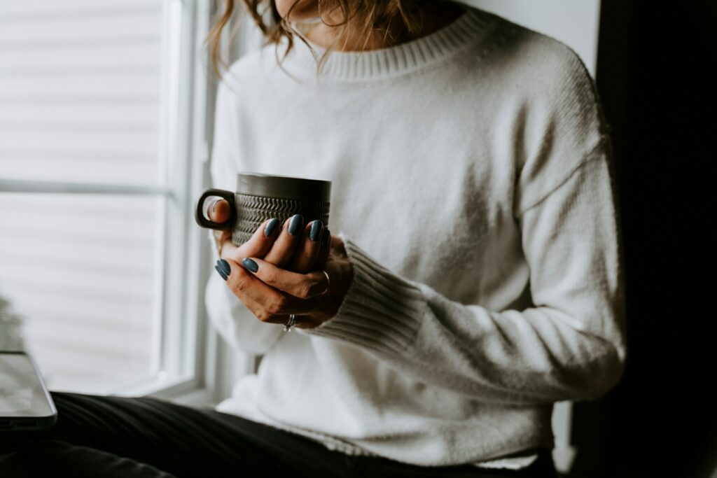 why self care feels impossible A woman holding a cup of coffee while looking at her laptop
