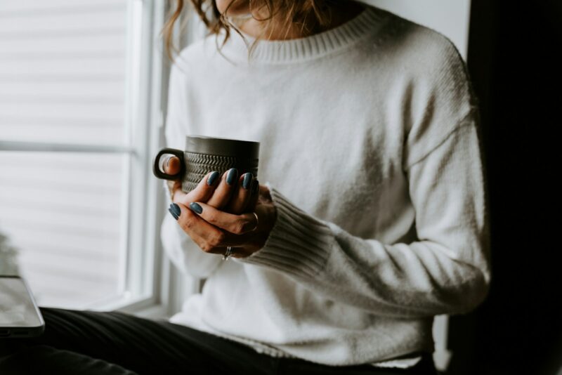 why self care feels impossible A woman holding a cup of coffee while looking at her laptop