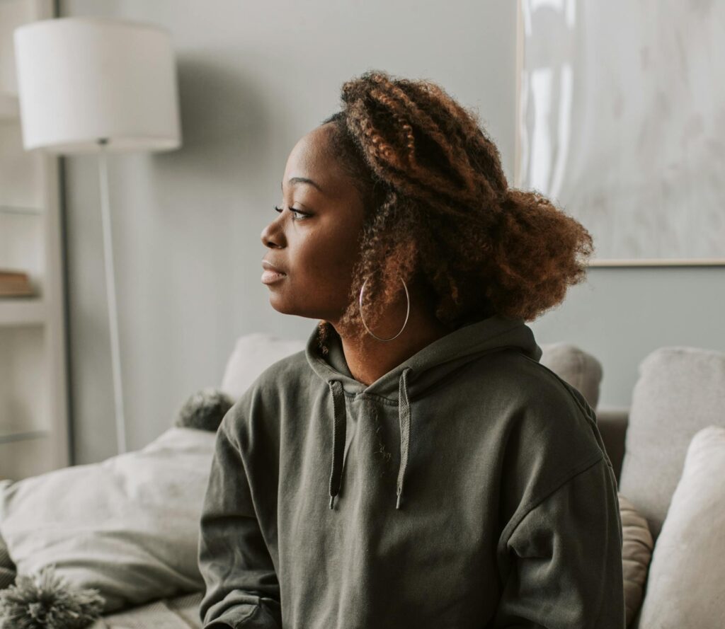understanding reactions as a woman in a hoodie sits on a sofa holding a cup, exuding a calm and relaxed vibe indoors.